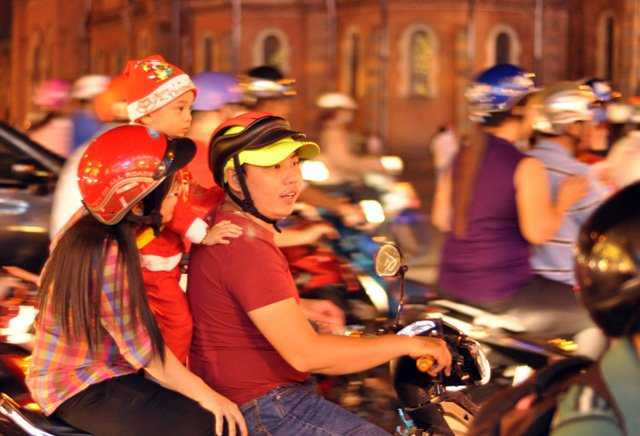 Nhiều em nhỏ mặc quầ áo, đội mũ ông già Noel được bố mẹ chở đi ngắm đường phố về đêm.