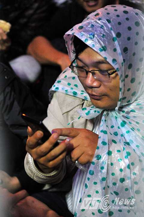 Đội áo mưa, ngồi chơi điện thoại giết thời gian nhưng tâm trạng chung của nhiều vị phụ huynh là không mua được vắc xin trong đợt này.