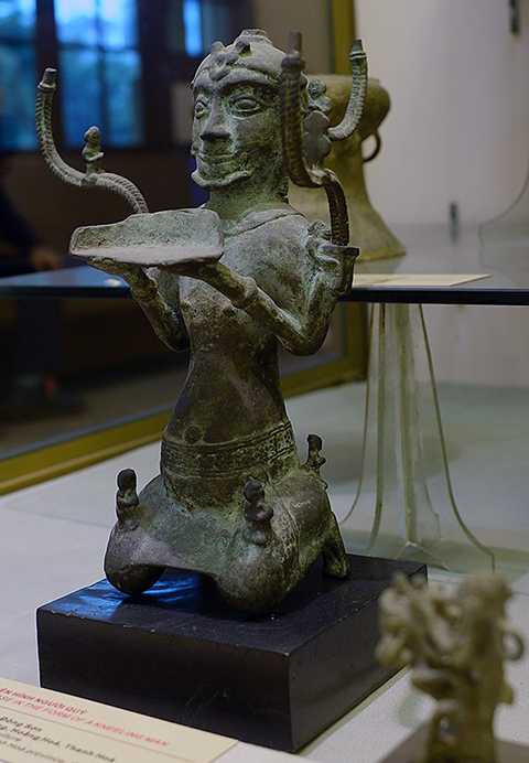 Cây đèn hình người quỳ là một trong 30 hiện vật đầu tiên được Thủ tướng công nhận là bảo vật quốc gia. Đèn cao 40 cm, rộng 27 cm, nặng 1,9 kg, có niên đại khoảng 1.700-2.000 năm. Cây đèn được phát hiện trong ngôi mộ số 3 ở Lạch Trường (Thanh Hóa), mang hình tượng một người đàn ông mình trần, đóng khố, hai tay nâng đĩa đèn trong tư thế quỳ. Trên đầu tượng được gắn vương miện, tóc để chỏm. Hai vai và sau tượng gắn 3 chữ S, mỗi chữ S đỡ một đĩa đèn và gắn một hình người đang quỳ. Trên hai đùi và đằng sau người đàn ông có 4 nhạc công cũng ở tư thế quỳ, hai nhạc công đang thổi sáo. Đây là cây đèn hình người lớn nhất trong số ít cây đèn cùng loại, thể hiện kỹ thuật đúc khéo léo và phản ánh thẩm mỹ cao của cư dân cổ thời kỳ hậu văn hóa Đông Sơn. Cây đèn hình người quỳ là một trong 30 hiện vật đầu tiên được Thủ tướng công nhận là bảo vật quốc gia. Đèn cao 40 cm, rộng 27 cm, nặng 1,9 kg, có niên đại khoảng 1.700-2.000 năm. Cây đèn được phát hiện trong ngôi mộ số 3 ở Lạch Trường (Thanh Hóa), mang hình tượng một người đàn ông mình trần, đóng khố, hai tay nâng đĩa đèn trong tư thế quỳ. Trên đầu tượng được gắn vương miện, tóc để chỏm. Hai vai và sau tượng gắn 3 chữ S, mỗi chữ S đỡ một đĩa đèn và gắn một hình người đang quỳ. Trên hai đùi và đằng sau người đàn ông có 4 nhạc công cũng ở tư thế quỳ, hai nhạc công đang thổi sáo. Đây là cây đèn hình người lớn nhất trong số ít cây đèn cùng loại, thể hiện kỹ thuật đúc khéo léo và phản ánh thẩm mỹ cao của cư dân cổ thời kỳ hậu văn hóa Đông Sơn.