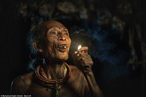 Người phụ nữ lớn tuổi ngồi hút điếu thuốc trong ngôi nhà lá treo đầy xương sọ động vật