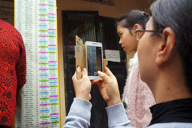 Sao xấu dán trên cột sẽ được tô màu nổi bật khác thường để mọi người dễ dàng nhận diện. Trong ảnh là một người phụ nữ dùng điện thoại chụp lại bảng sao chiếu mệnh để làm lễ cho cả gia đình trong ngày đầu năm mới.