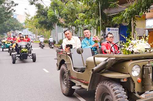 Chú rể mặc áo dài xanh, cầm hoa ngồi xe jeep dẫn đầu lễ rước dâu.