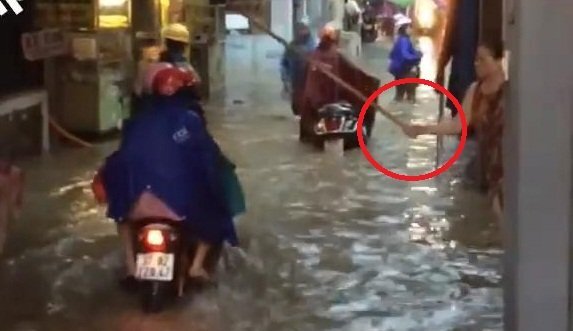Clip: Người phụ nữ đứng trên phố ngập, lăm le cầm gậy vụt người đi đường