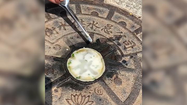 Người đàn ông nướng bánh trên nắp cống giữa nắng nóng như thiêu đốt