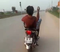 Quái xế đầu trần, nằm dài ra yên lái xe máy lao vun vút bằng chân