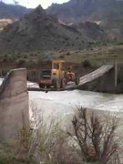 Máy xúc lò dò đi qua cầu treo tạm bợ