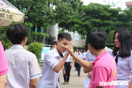 Thầy cô mặc đồng phục màu hồng đứng trước cổng, chào đón học sinh hoàn thành bài thi