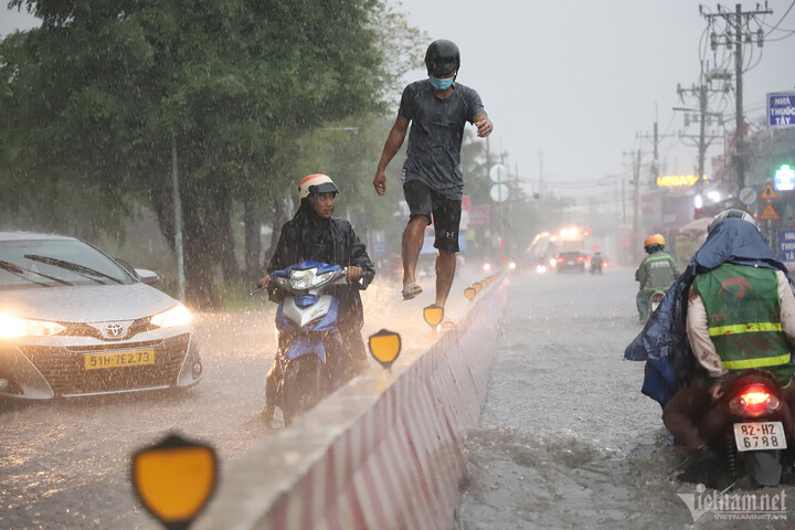 Nước ngập sâu trên đường Nguyễn Xiển, một người đàn ông chọn cách bước trên dải phân cách để đi qua.