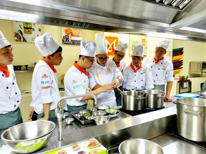 Giảng viên Lưu Huỳnh Châu đứng thứ 3 từ trái qua hướng dẫn các học trò chế biến món ăn.
