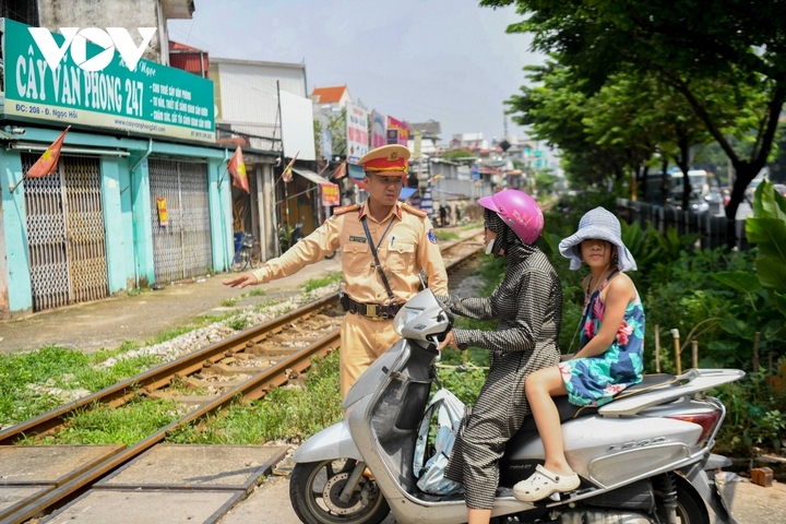 Cán bộ CSGT Đường sắt hướng dẫn người dân đi qua điểm giao cắt đường sắt an toàn. (Ảnh: VOV.VN).