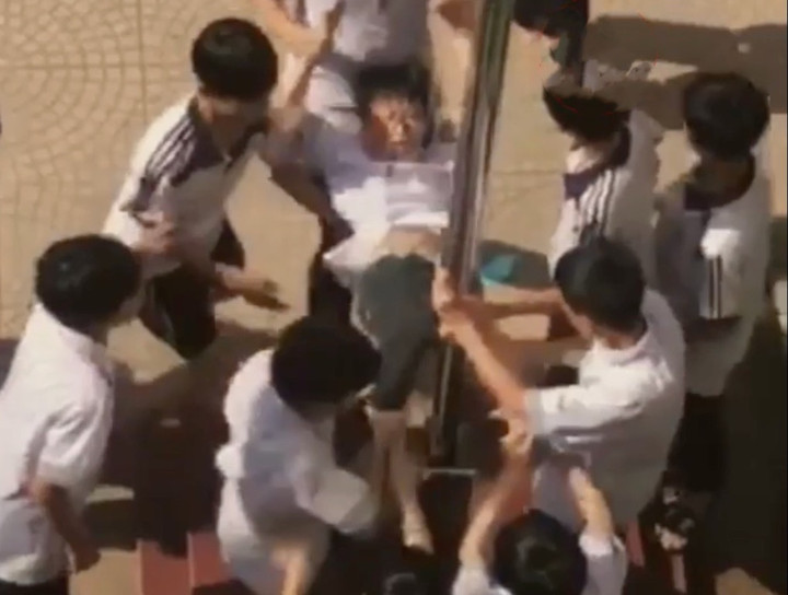 Nam sinh bị các bạn kéo tay, chân ép vùng kín vào cột cờ. (Ảnh cắt từ clip)
