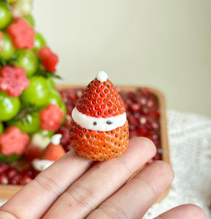 Ông già Noel mini được làm bằng dâu tây. Chị Thủy cắt bớt phần cuống để quả dâu có độ thăng bằng khi đặt xuống, tiếp đó cắt làm đôi, phần đế dày nhỉnh hơn phần mũ. Sau đó, chị dùng sốt mayonnaise để tạo hình mặt, mũ và lấy 2 hạt vừng làm mắt. (Ảnh: Cao Thanh Thủy)