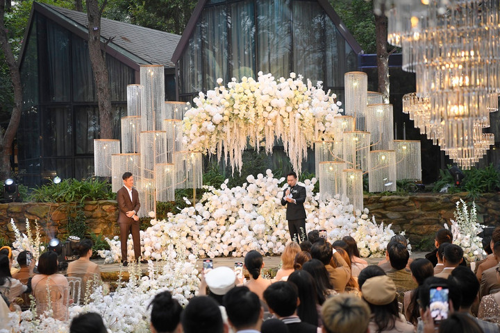 Từ sân khấu đến lối dẫn đều được trang trí bằng hoa trắng tinh khôi, sang trọng. Xen kẽ cụm hoa là những cột đèm chùm pha lê rủ lấp lánh.