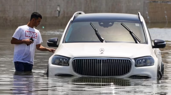 Một người đàn ông đứng cạnh chiếc ô tô ngập trong nước sau trận mưa lớn ở Dubai, UAE, ngày 19/4. (Ảnh: Reuters)