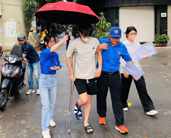 Một sĩ tử khác gặp tình trạng tương tự cũng được chăm sóc tận tình tại điểm thi THPT Phan Huy Chú (Đống Đa). Nam sinh chống nạng chân vừa được dìu, vừa được che ô tránh thời tiết nắng.