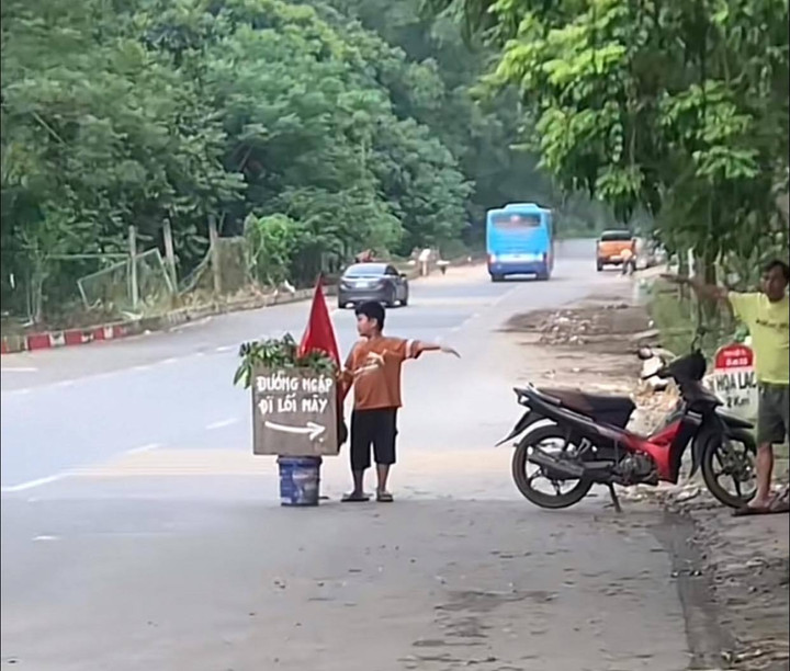 Cậu bé chỉ dẫn đường cho người đi xe máy tránh bị ngập. (Ảnh: Minh Nguyễn)