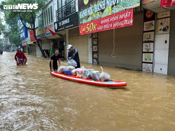 Một người dân ở Phúc Xá, phường duy nhất của quận Ba Đình nằm ngoài đê sông Hồng, sử dụng thuyền kayak chở đồ ăn trên phố bán cho các nhà dân đang mắc kẹt trong nước lũ. Đồ ăn trên chiếc thuyền gồm bánh mỳ, cơm hộp,...