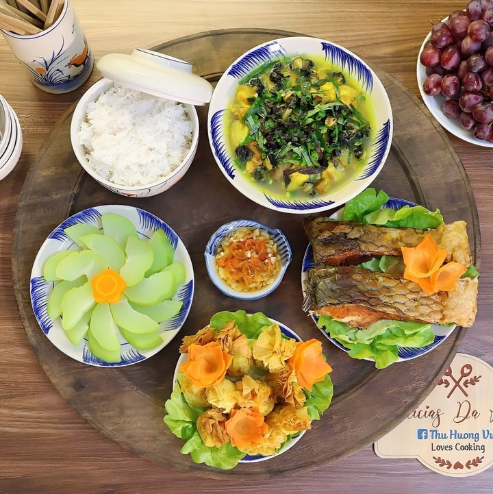 Mâm cơm gồm các món ốc om chuối đậu, cá chép sông rán giòn, chả giò nhân gà ngô non, su su luộc, tráng miệng bằng nho đỏ kẹo.