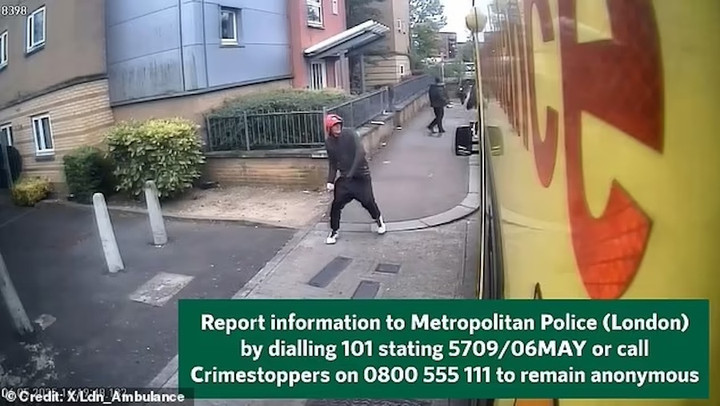 Người đàn ông lại gần xe cứu thương trong bộ đồ tối màu, mũ đỏ và giày trắng.