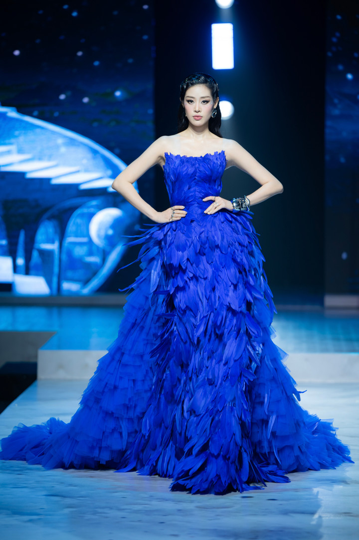 Sau hơn nửa năm lên xe hoa, Hoa hậu Khánh Vân vừa có màn tái xuất rực rỡ tại sàn diễn thời trang, khẳng định đẳng cấp và sức hút không hề thuyên giảm sau khi kết hôn. Người đẹp 9X đảm nhận vai trò vedette. Trong đêm diễn, Khánh Vân khoác lên mình chiếc váy ôm sát đính kết hàng trăm chiếc lông vũ màu xanh đặc trưng. Dù diện bộ váy cồng kềnh, Hoa hậu Hoàn vũ Việt Nam 2019 vẫn thể hiện thần thái kiêu sa, bước đi uyển chuyển đầy bản lĩnh, nhận tràng vỗ tay không ngớt từ khán giả.