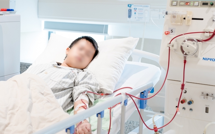 Đạt nằm lặng lẽ bên chiếc máy lọc máu, khuôn mặt xanh xao, ánh mắt mệt mỏi. (Ảnh: Phượng Lê)
