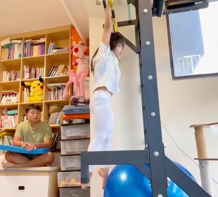 Cô bé bắt chước động tác bơi ngửa bằng cách sử dụng thiết bị tập thể dục mà bố lắp đặt tại nhà để rèn luyện các cơ cần thiết khi bơi. (Ảnh: Handout)