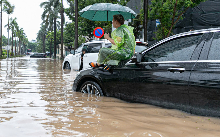 Người đàn ông lái xe con phải trèo lên nóc capo, ngồi hơn 2 tiếng chờ cứu hộ. Xung quanh anh, hàng loạt xe khác cũng nằm bất động, giao thông tắc nghẽn kéo dài.