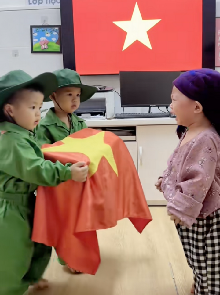 Hai bé trai mặc bộ quân phục màu xanh lá nhập vai chiến sỹ, còn bé gái trong bộ đồ hoa, đóng vai người mẹ.