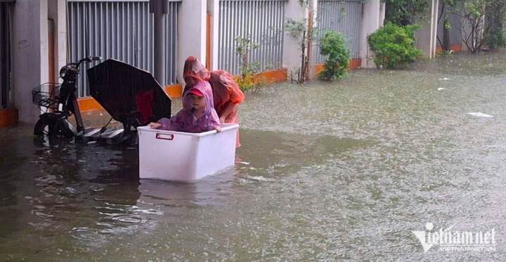 Một phụ huynh mang thùng đến trường, cho con ngồi vào thùng để tránh bị ngập nước.