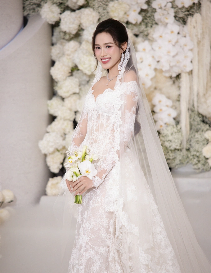 Cô dâu Đỗ Thị Hà xuất hiện trong chiếc váy ren trắng ôm sát, kết hợp với voan dài hàng mét, cầm bó hoa phong lan trắng tinh tế.