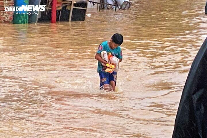 Một bé trai lội nước lũ cả cây số để nhận đồ ăn từ các đơn vị thiện nguyện.