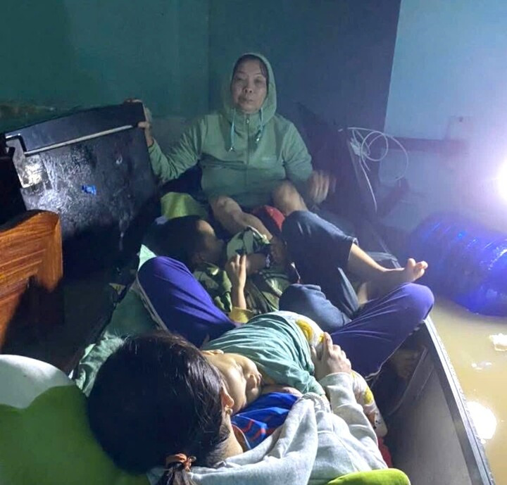 Trẻ em và người già ngồi trên xuồng chống chọi với cơn lũ.