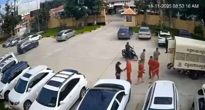 Hình ảnh lại cảnh một phụ nữ đội mũ lưỡi trai đứng chờ tại bãi xe tòa án và bí mật trao súng cho nhóm phạm nhân khi họ vừa bước xuống xe. (Ảnh: Khmer Times)