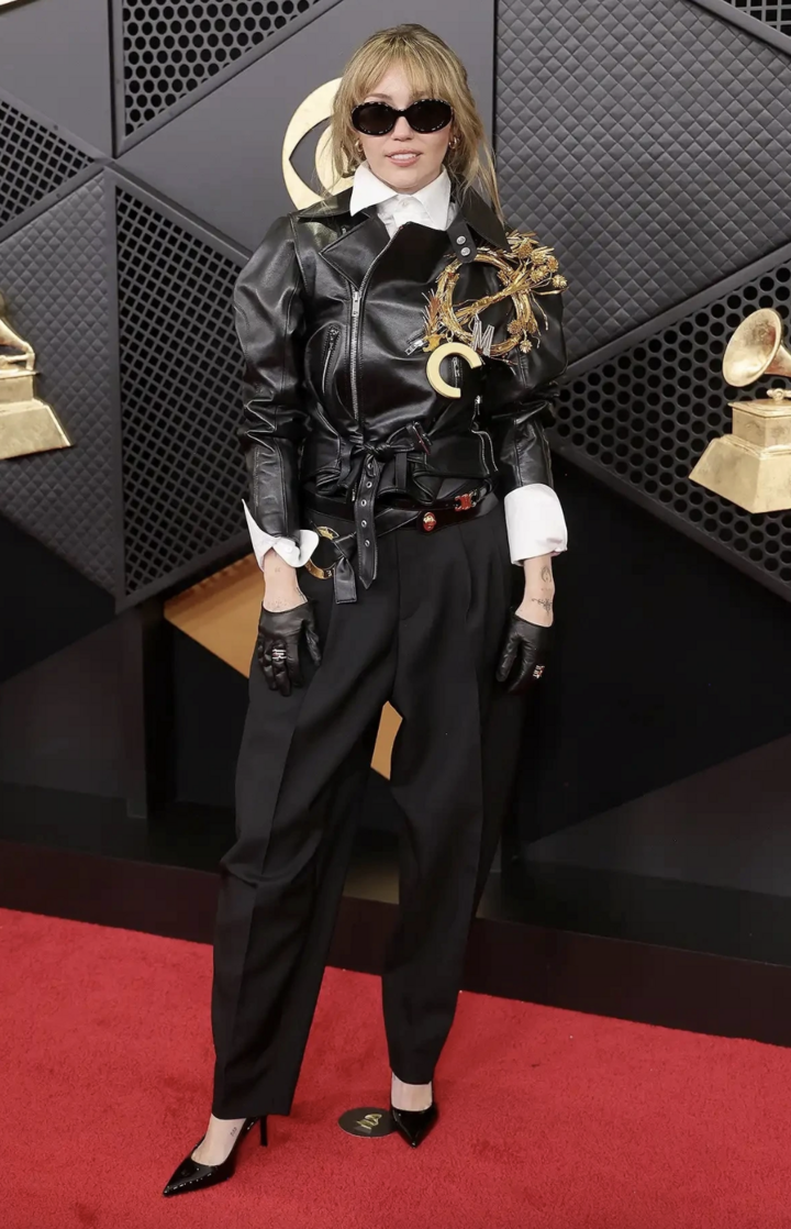 Miley Cyrus cá tính khi kết hợp quần tây đen và áo khoác da, điểm nhấn là chiếc trâm cài vàng ngoại cỡ. Nữ ca sĩ hoàn thiện bộ trang phục Celine bằng găng tay đen và kính râm. (Ảnh: WireImage)