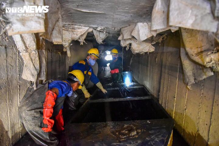 Một tổ công nhân làm việc trong cống ngầm chật hẹp, phối hợp gỡ rác tại song chắn để khơi thông dòng chảy, bảo đảm hệ thống vận hành thông suốt dịp Tết.