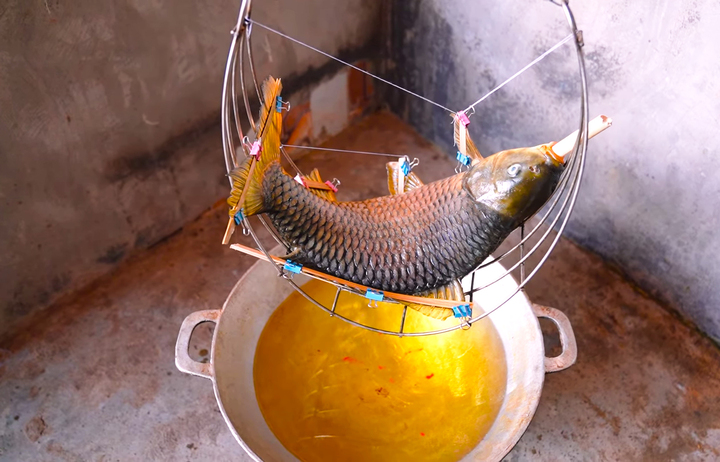 Sau khi được định hình xong, cá chép để vào cái võng bằng inox khoảng gần một giờ cho cá se lại. Tiếp đó, khoảng 5 lít dầu ăn hoặc mỡ lợn được đổ vào chảo to sâu lòng đun nhỏ lửa cho sôi lăn tăn, võng cá đặt phía trên cách mặt chảo khoảng chừng 10-15cm.