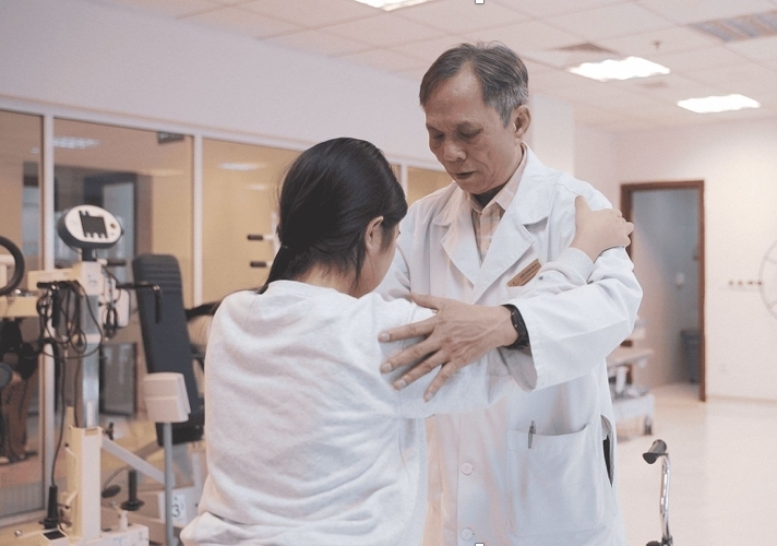 Bé gái chập chững tập đi dưới sự hướng dẫn của bác sĩ phục hồi chức năng.