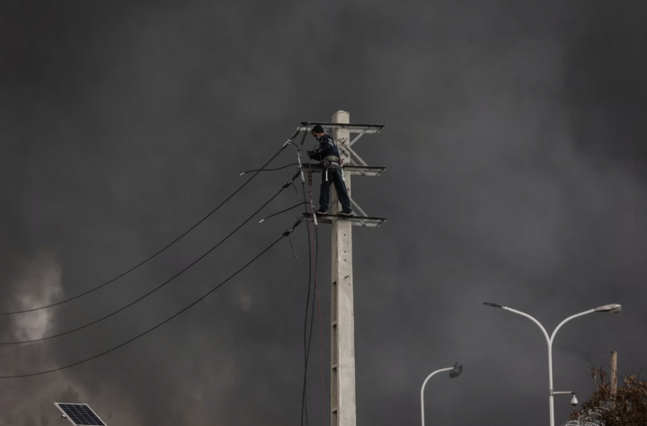 Người đàn ông sửa cột điện khi khói bốc lên sau vụ tấn công tại Tehran.