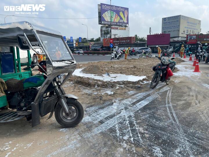 Các công nhân đổ cát lên các mảng sơn tràn để thấm hút và làm sạch mặt đường.