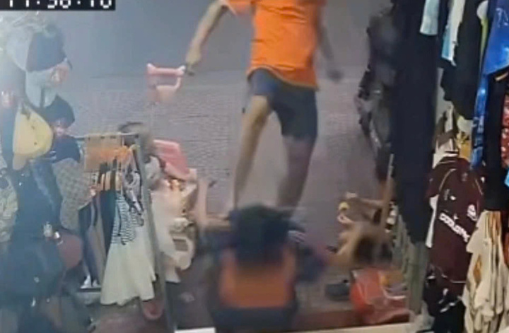 Gã đàn ông mặc áo cam đá vào mặt người phụ nữ đang trông 2 con nhỏ.