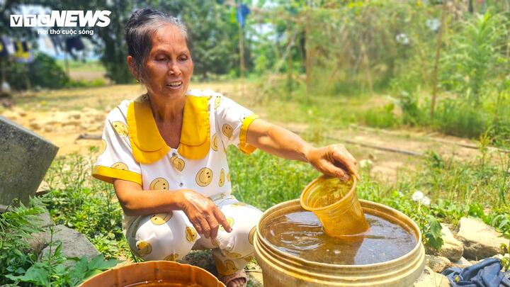 Bà Nông Thị Biến bên 2 thùng nước múc lên từ giếng nhà mình bị nhiễm phèn nghiêm trọng, nổi ván lềnh bềnh.