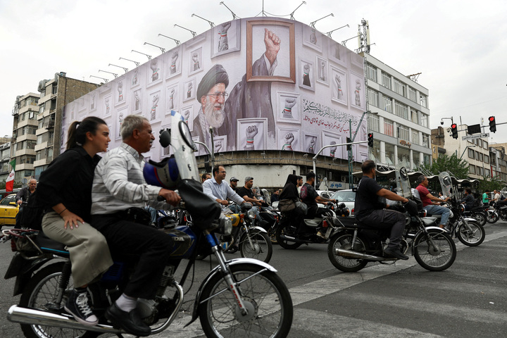 Người dân đi xe máy ngang qua tấm biển có hình ảnh Lãnh tụ tối cao quá cố của Iran, Đại giáo chủ Ali Khamenei, tại Tehran ngày 5/5. (Ảnh: WANA/Reuters)