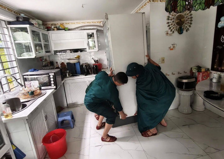 Lực lượng chức năng hỗ trợ người dân di dời thiết bị điện, tài sản có giá trị khỏi khu vực ngập úng.
