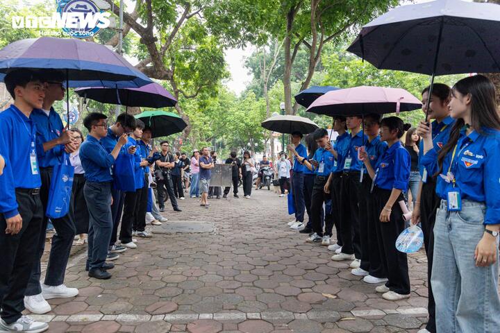 Các tình nguyện viên đội mưa, cầm ô hỗ trợ và che chắn cho thí sinh trước cổng điểm thi.