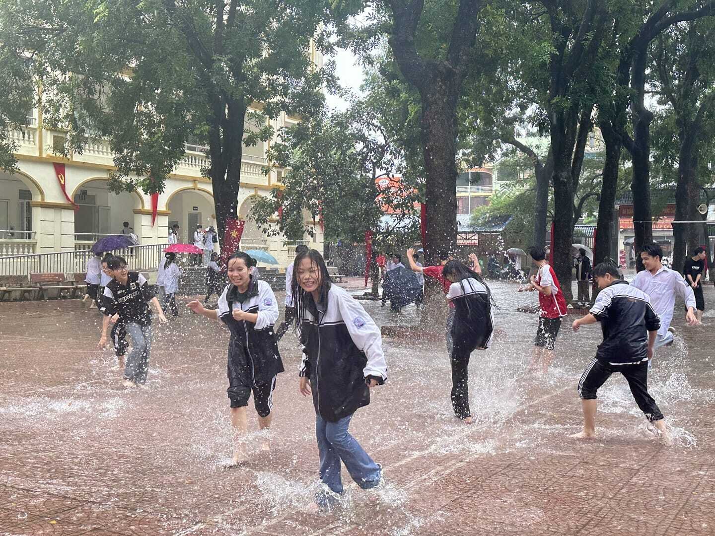 Học sinh THPT Thạch Thất ùa xuống sân trường chơi đùa trong cơn mưa tầm tã. Các em thư giãn, vui vẻ tận hưởng khoảnh khắc đặc biệt này. (Ảnh: Châu Kiều Nhi)