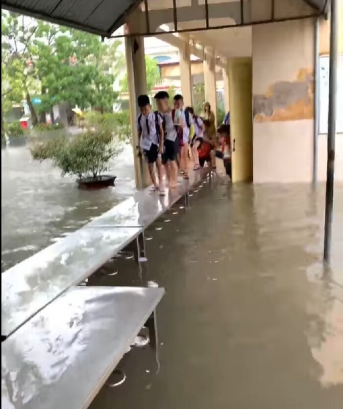 Nước ngập sâu, giáo viên lấy bàn từ bếp ăn bán trú kê sát nhau tạo thành đường đi cho học sinh (Ảnh chụp màn hình)