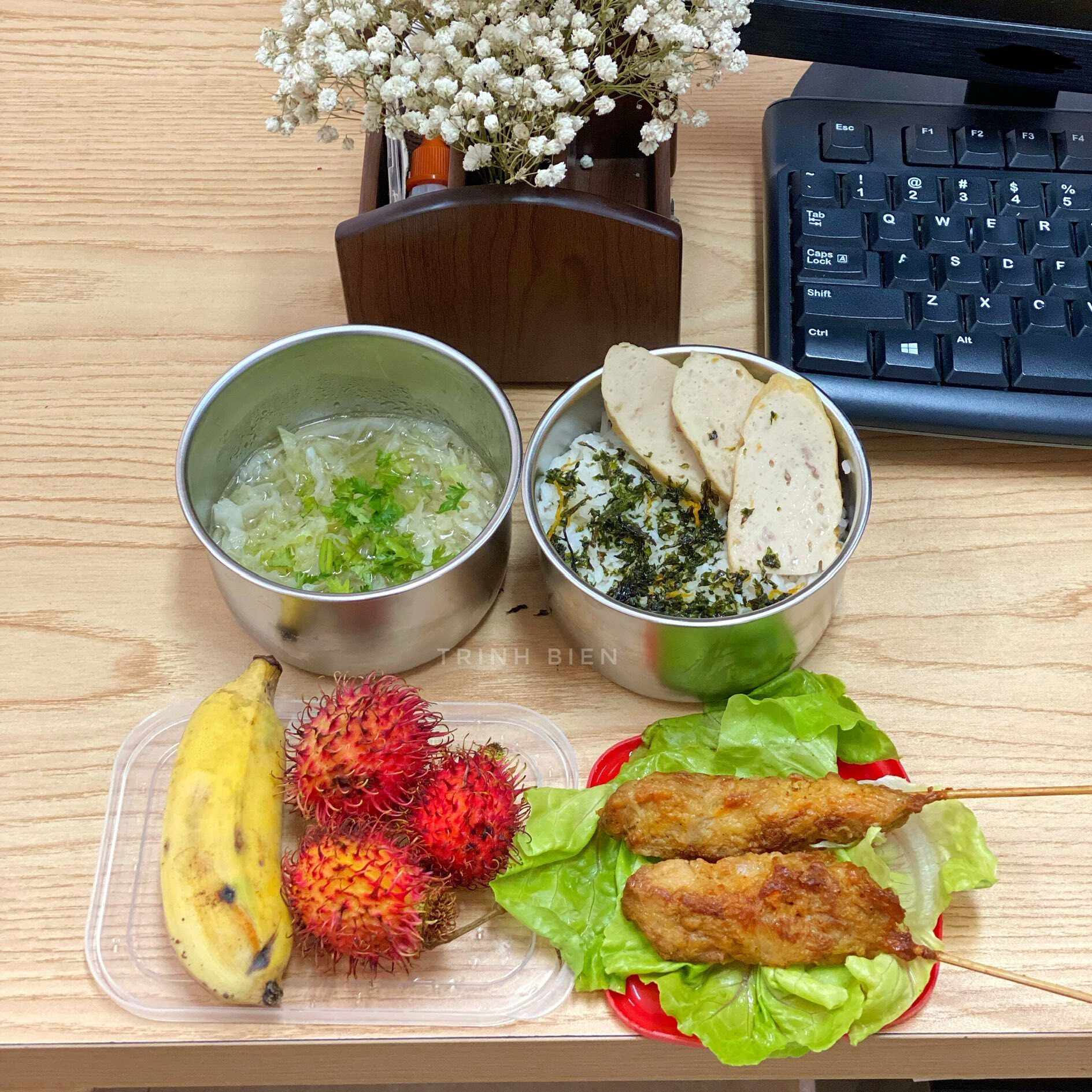Bữa trưa công sở gồm món thịt xiên gà, chả bìa, bắp cải xanh nấu canh, tráng miệng với chuối, chôm chôm.