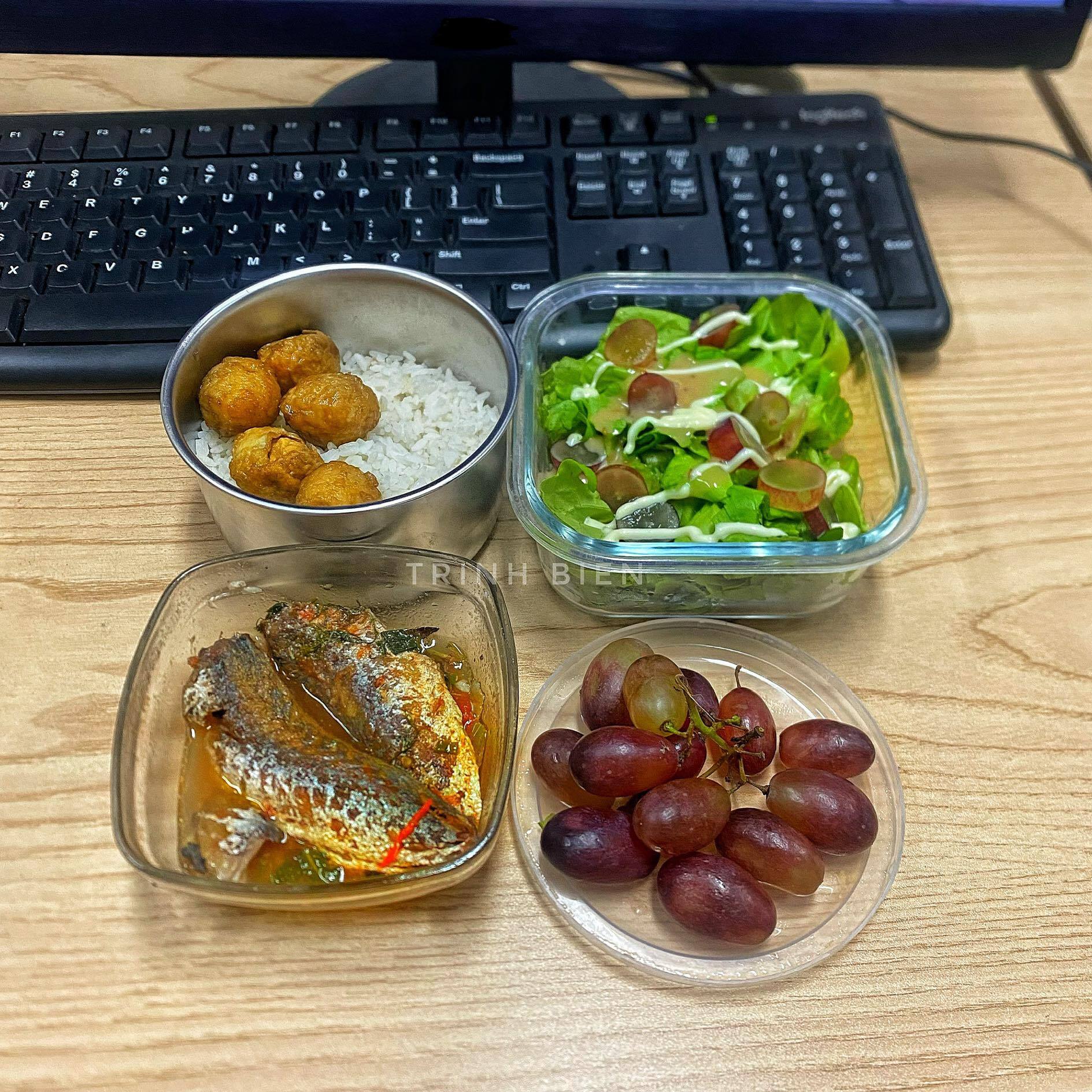 Hộp cơm này có cá nục sốt cà chua, salad rau xanh và nho ngọt.