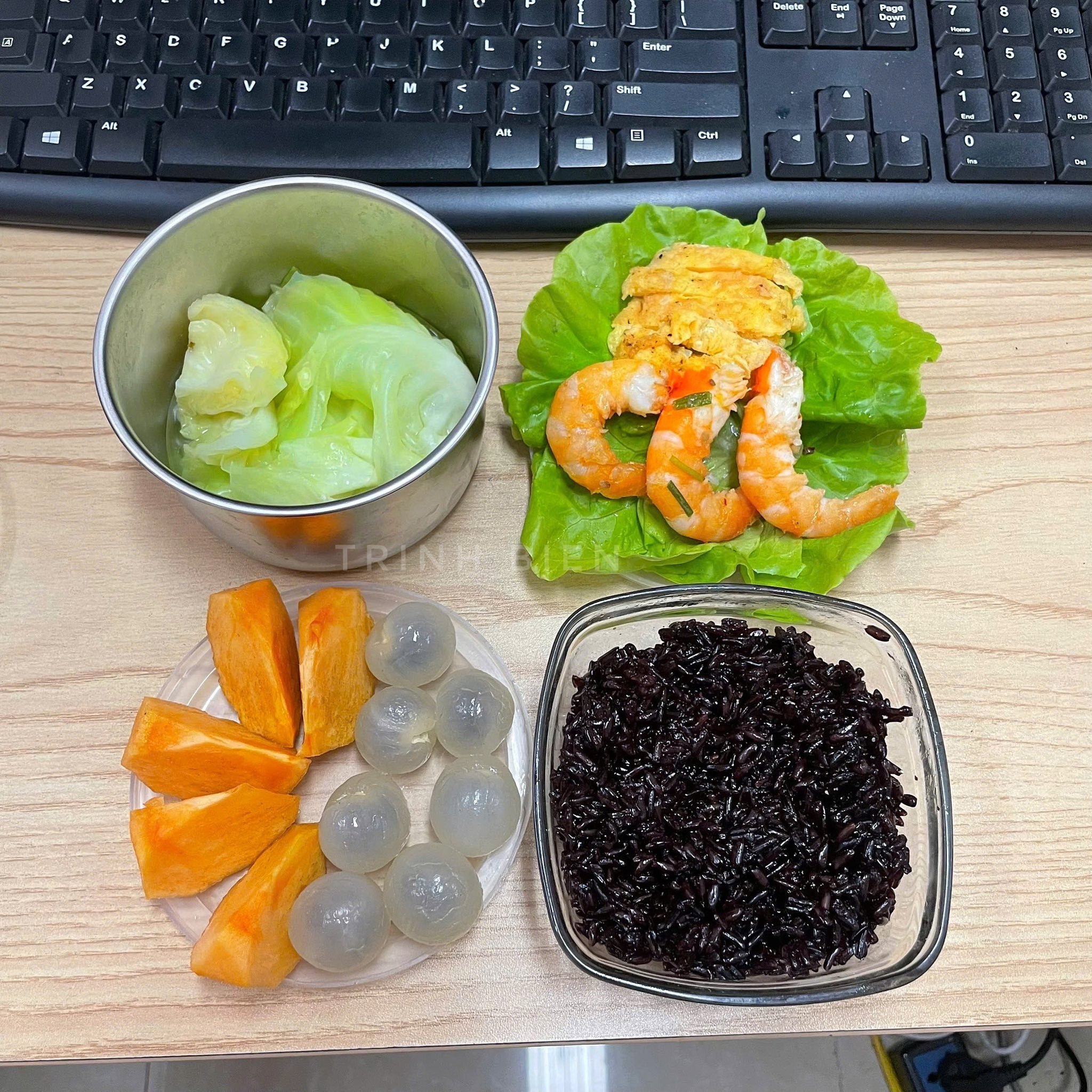 Hộp cơm có món tôm hấp, trứng rán vàng ươm, bắp cải luộc và tráng miệng với nhãn, hồng giòn.