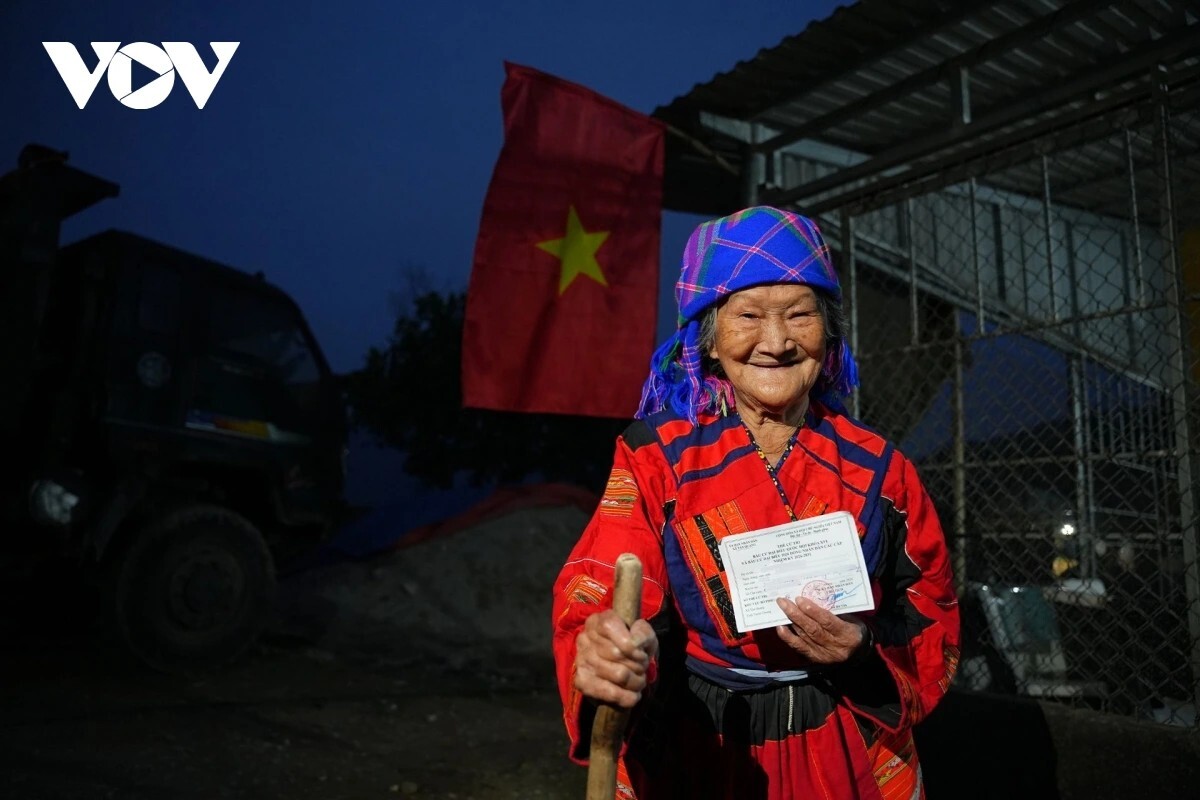 Một số hộ gia đình đi làm vắng nhà, lực lượng làm nhiệm vụ phải quay lại vào chiều tối để trao thẻ cử tri tận tay từng người. Cụ bà Làn Lở Mẩy, 85 tuổi, trong bộ trang phục truyền thống của dân tộc Pà Thẻn hạnh phúc khi cầm trên tay tấm thẻ cử tri, tấm phiếu thực hiện quyền công dân của mình.